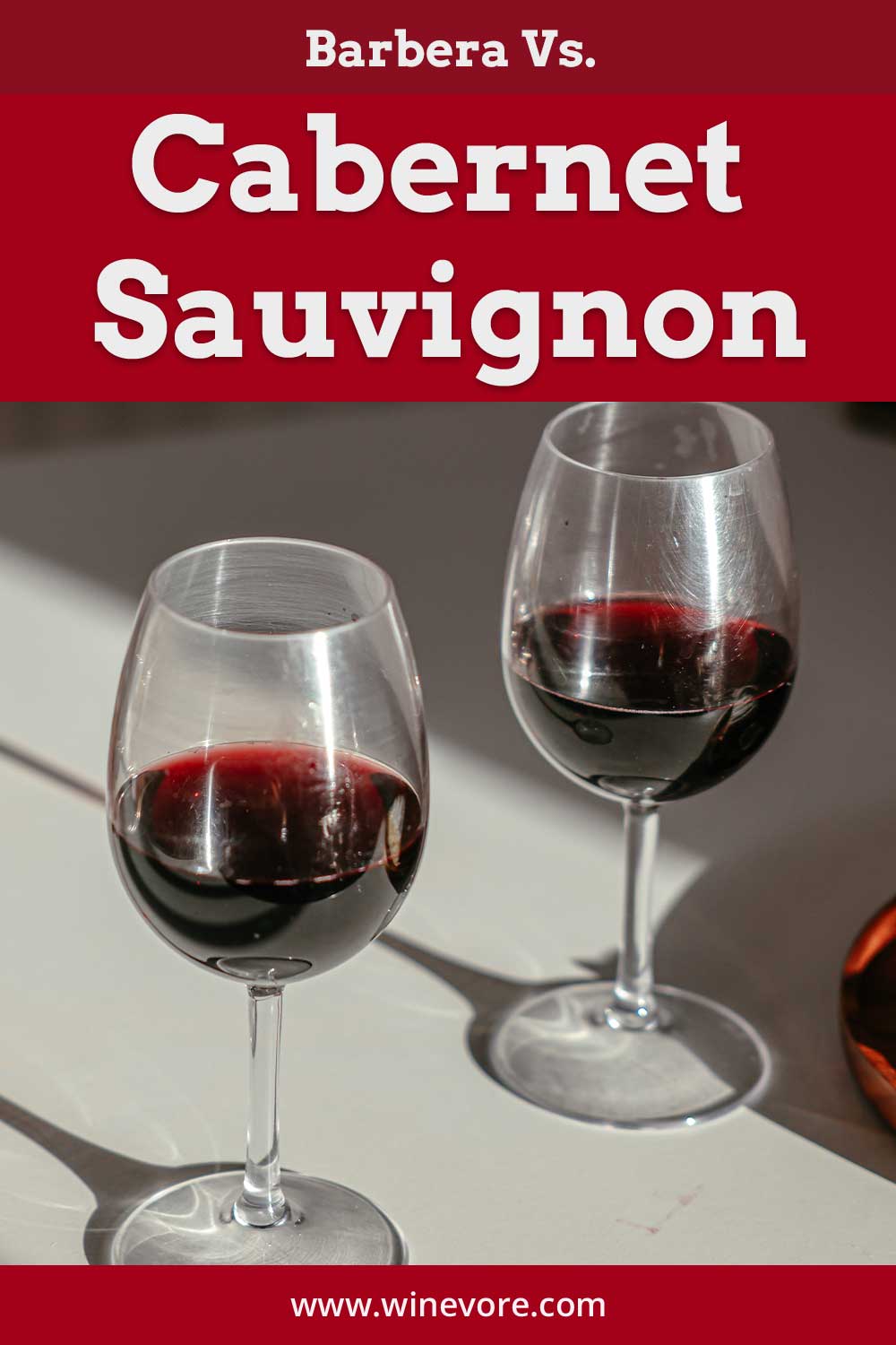 Two glasses of red wine on a white surface - Barbera Vs. Cabernet Sauvignon.