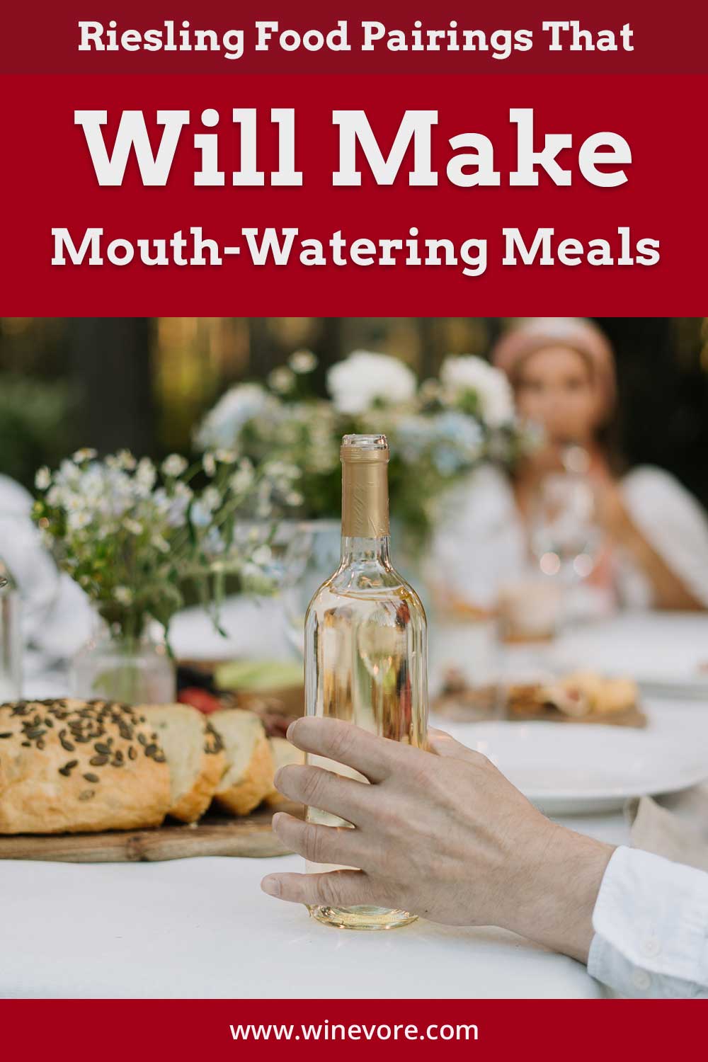 Person's hand holding a wine bottle in front of a table - Riesling Food Pairings.