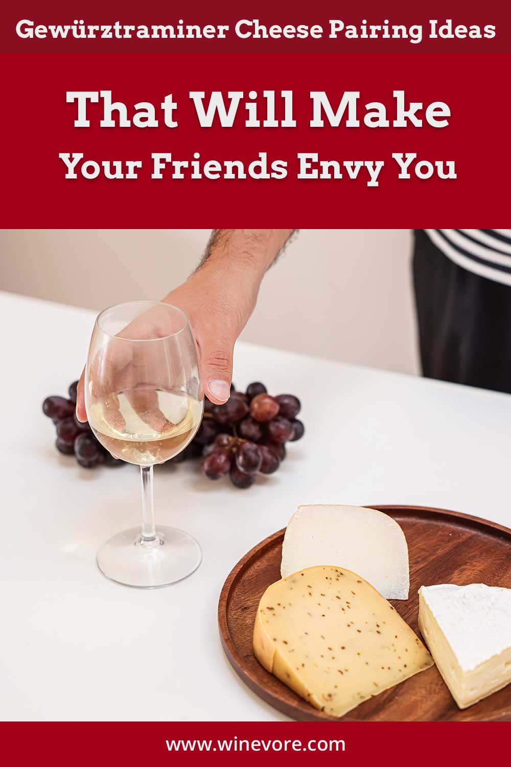 Person's hand grabbing a wine glass from a table with grapes and cheese on it - Gewürztraminer Cheese Pairing Ideas.