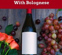 A wine bottle with some grapes and flowers on a wooden surface - Dry Red Wine With Bolognese.