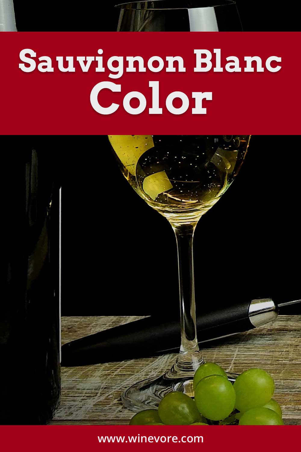 Wine glass full of white wine on wooden surface, a wine bottle and grapes beside it - Sauvignon Blanc Color.